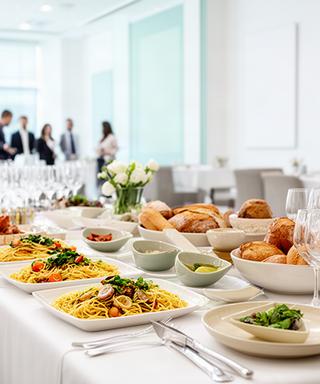 Buffet aziendale con vassoi di pasta fresca e verdure su tavoli in una sala luminosa