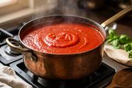 Pentola di rame con sugo di pomodoro che cuoce lentamente su un fornello