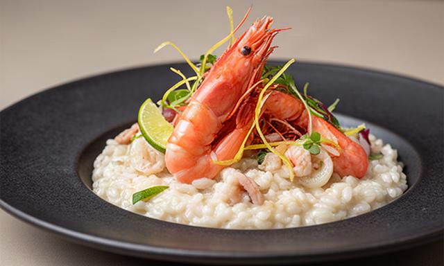 Risotto cremoso con gamberi rossi e lime servito su piatto scuro